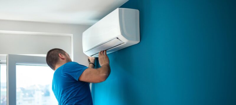 man in a blue shirt installing a ductless ac unit to a blue wall