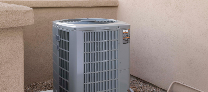 a gray outdoor ac unit installed in a corner with walls on three of its sides